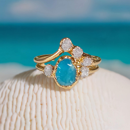 Raw Peruvian Opal and diamond engagement ring set on a seashell foreground with ocean backdrop.