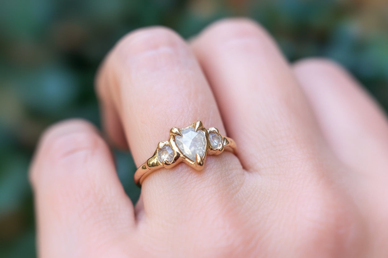 Rustic solid gold engagement ring featuring Salt & Pepper diamonds, showcased on a hand with greenery in the background.