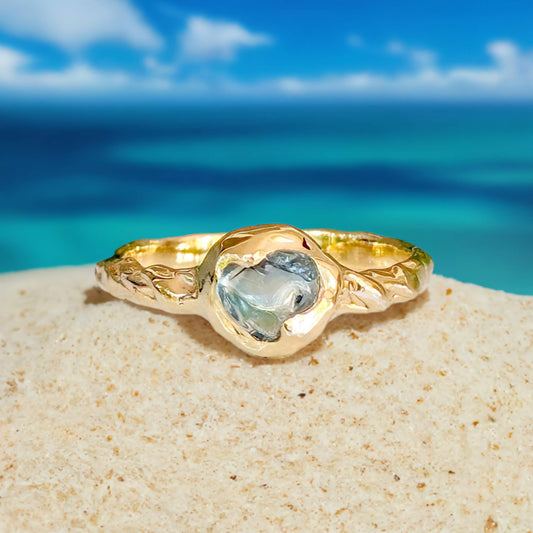 Australian sapphire ring in solid 14k gold with textured band, set against a beach backdrop.