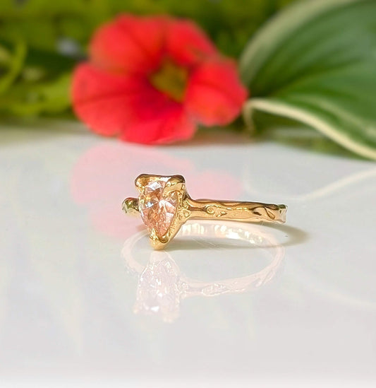 Peach Morganite pear-shaped ring in solid 14k gold with textured band, displayed against vibrant floral background.