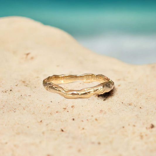Molten Gold stacking band on beige sand, showcasing its organic texture and unique design in solid 14k gold.