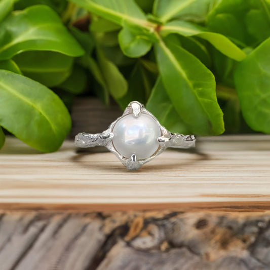 Textured sterling silver ring featuring a creamy-white Freshwater Keshi pearl, set against green foliage.