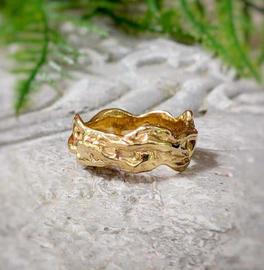 Textured Molten Gold wedding ring showcasing an abstract, nature-inspired design on a stone background.