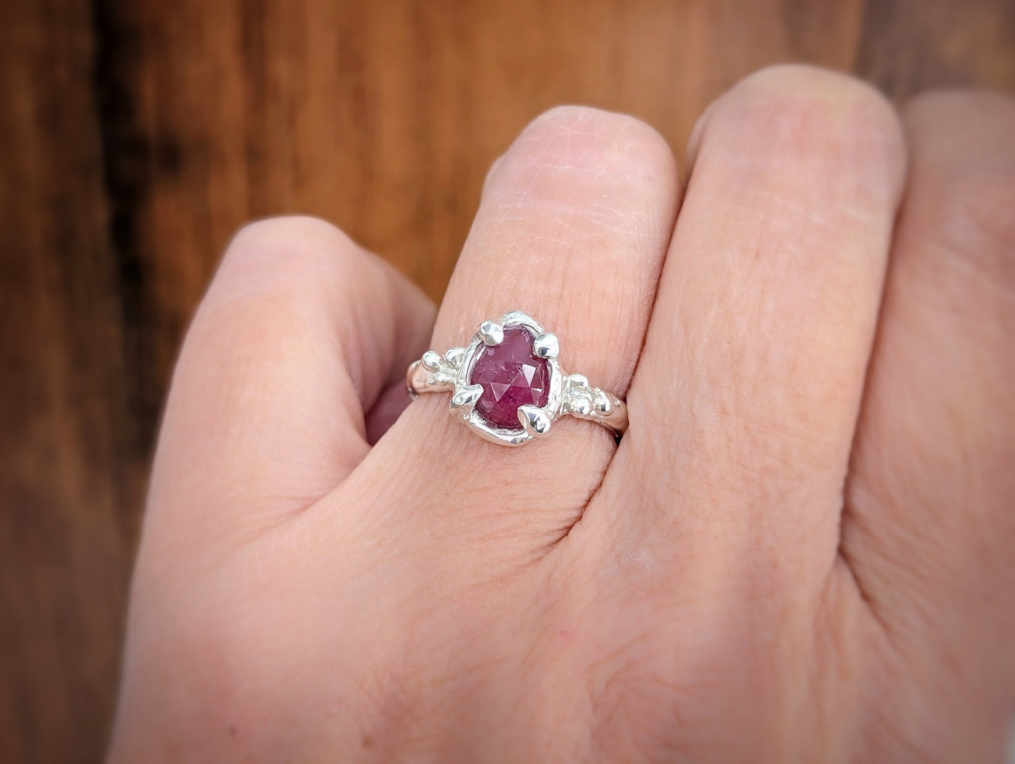 Hand wearing a textured Pink Sapphire engagement ring in sterling silver, featuring a pear-shaped rose cut gem.