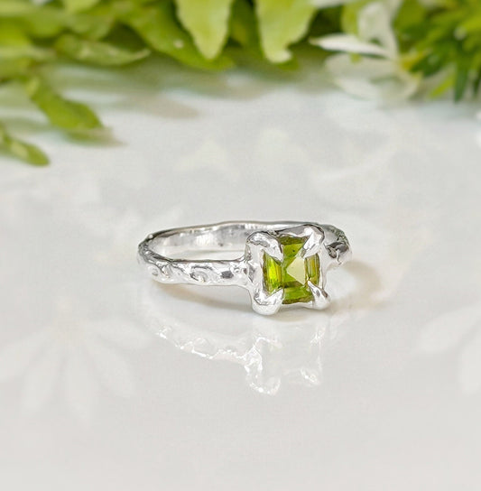 Solid silver Peridot ring with organic textured band and princess-cut green crystal, perfect for symbolizing love.