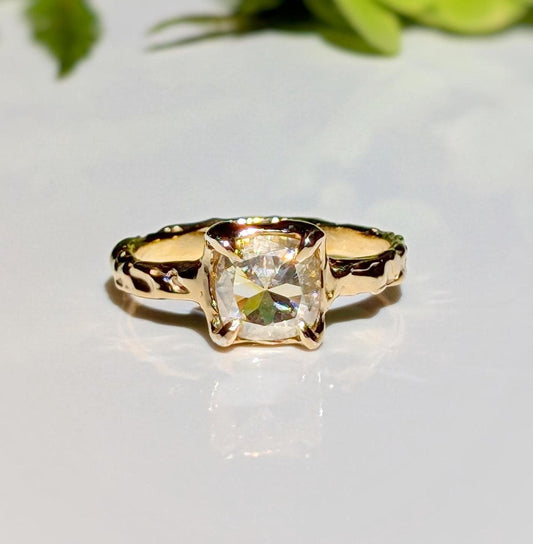 Moissanite engagement ring with 8mm cushion cut stone in textured 14k gold setting, showcasing timeless beauty.