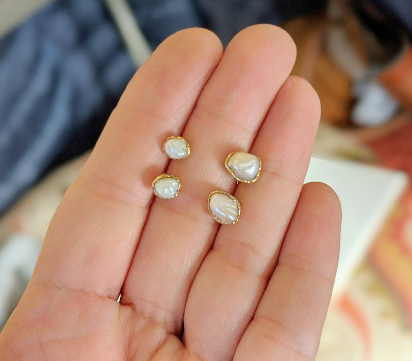 Hand holding two pairs of Freshwater Keshi Pearl stud earrings with gold settings.