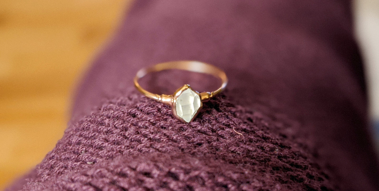 Raw Herkimer diamond engagement ring on a knitted surface, showcasing its delicate gold band and unique gemstone.