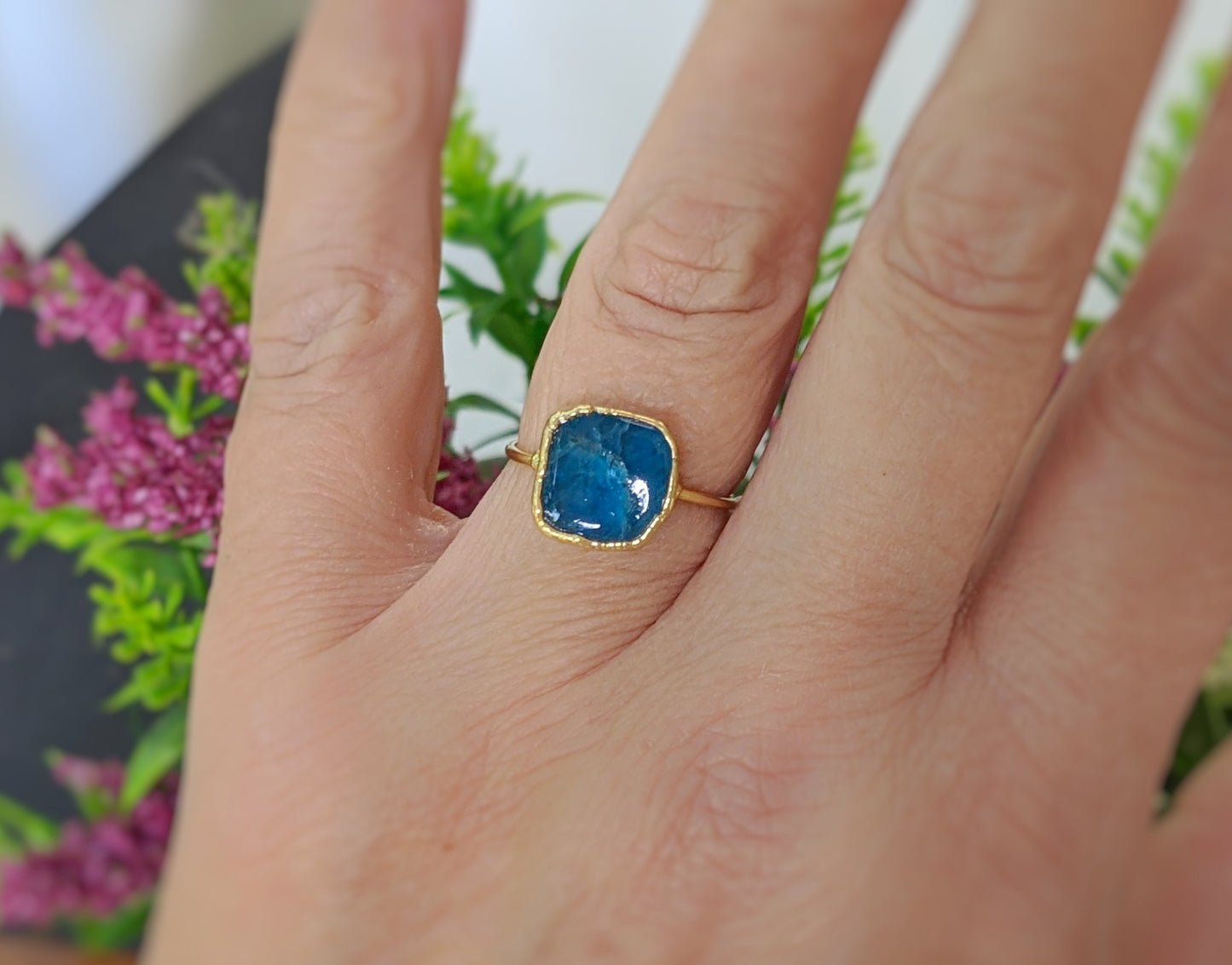 Natural blue Apatite ring on hand, set in 14k Gold filled band, surrounded by floral background.