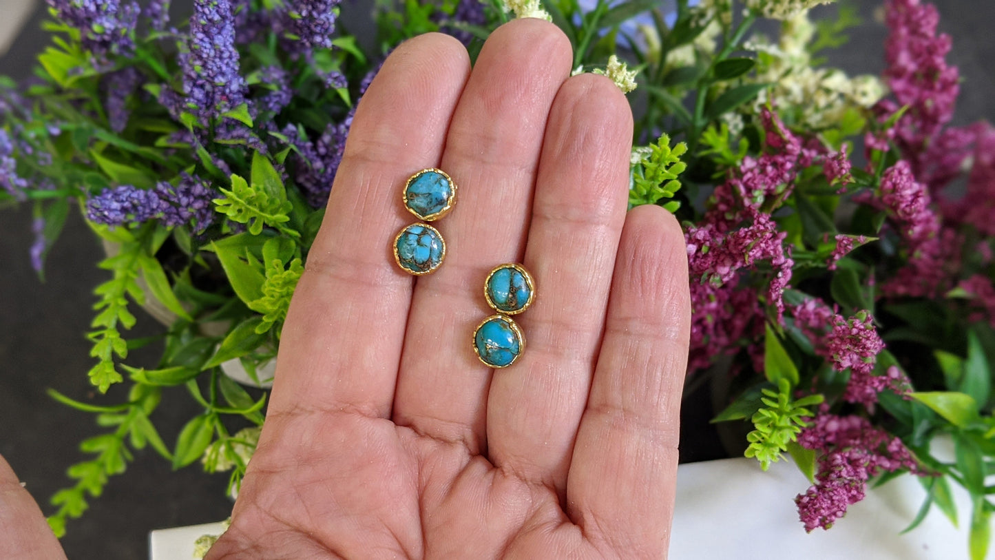 Turquoise stud earrings displayed in hand with colorful flowers in the background, showcasing their elegant design.