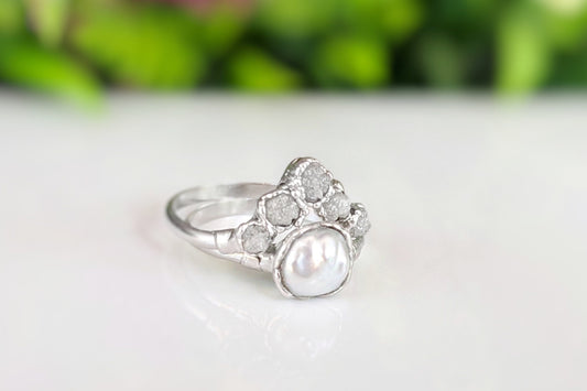 Keshi pearl and raw diamond chevron wedding ring set on a blurred floral background, showcasing unique handcrafted design.