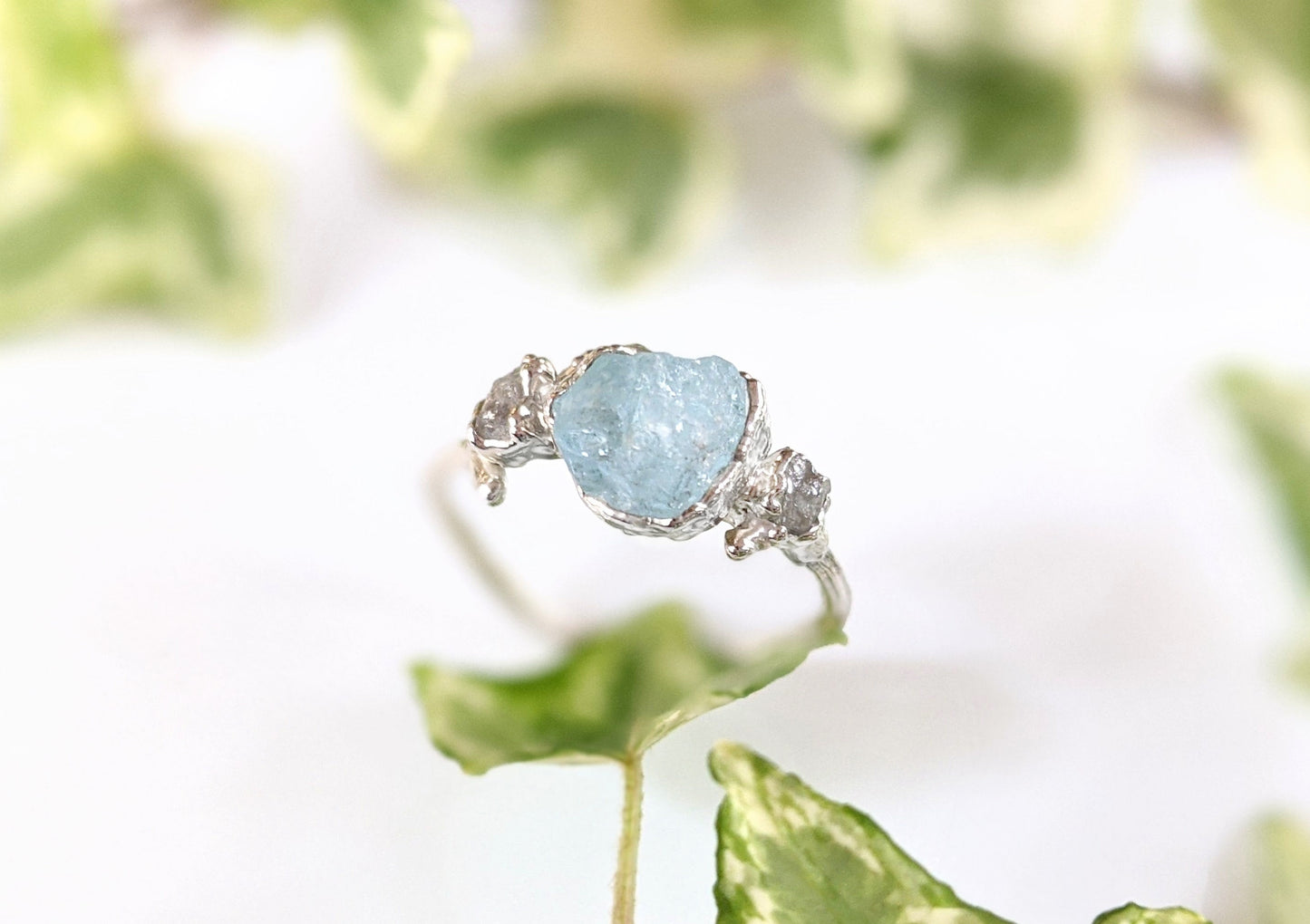 Raw Aquamarine and diamond twig ring on sterling silver band with greenery in background.