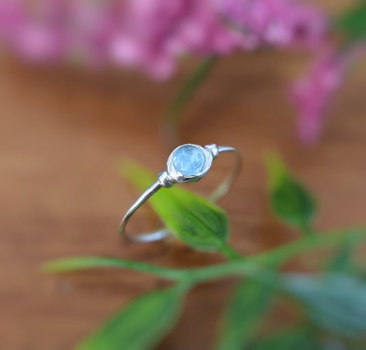 Dainty blue topaz stacking ring on a natural wooden surface with greenery in the background.