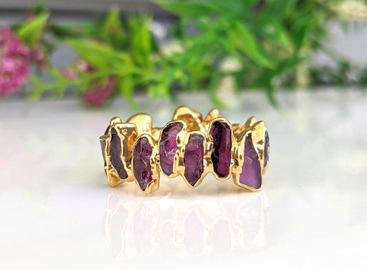 Raw Rhodolite Garnet eternity ring on a reflective surface, showcasing its unique gold-filled design and colorful gemstones.