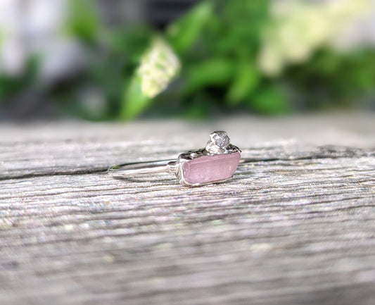 Handcrafted raw pink tourmaline and rough diamond ring on a wooden surface, symbolizing rustic elegance and love.