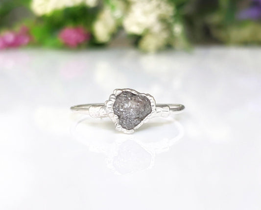 Raw uncut grey diamond engagement ring on a sterling silver band with floral background.