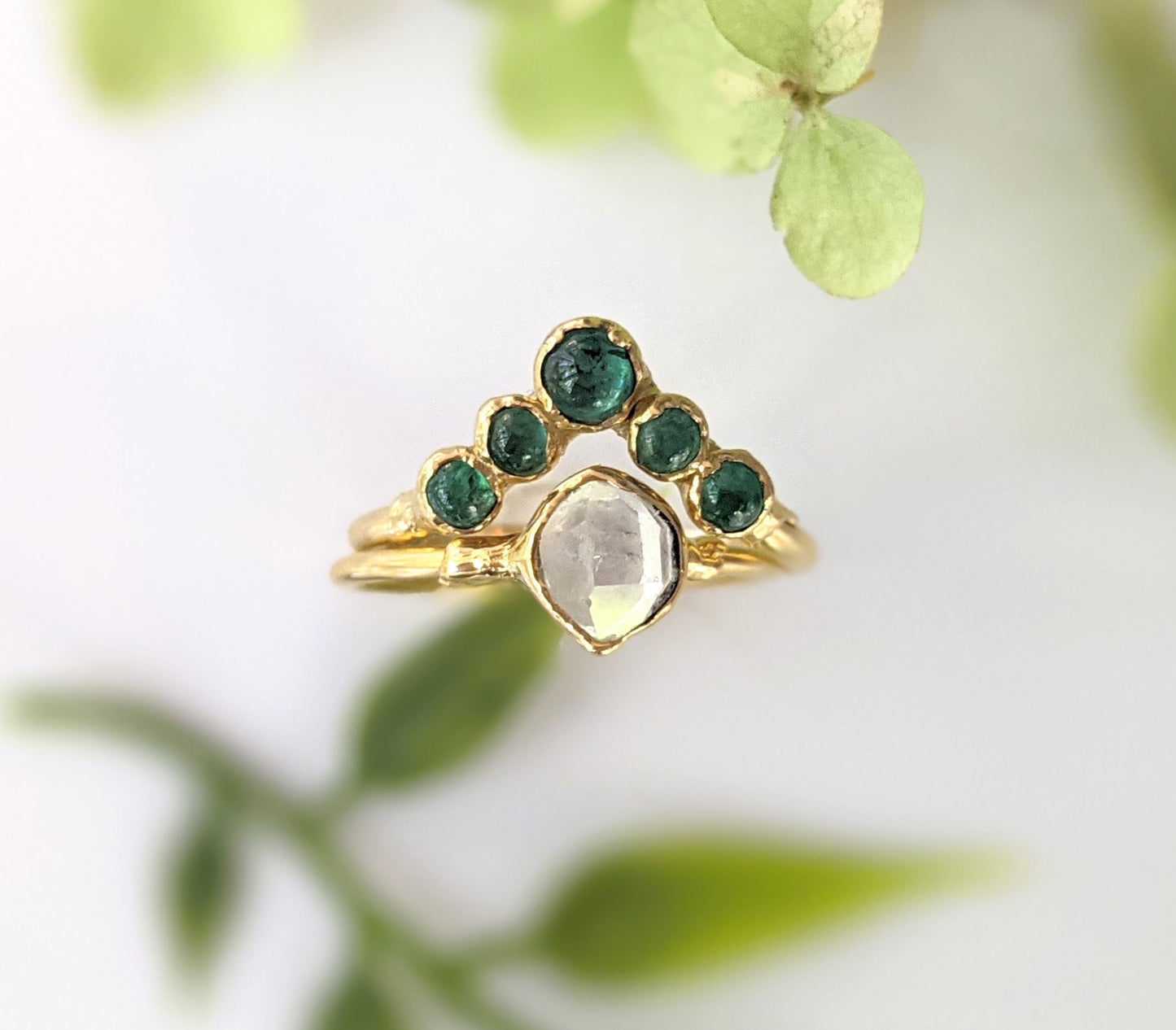 Natural Emerald Chevron wedding ring in 18k Gold featuring a unique design with green emeralds and a clear gemstone centerpiece.