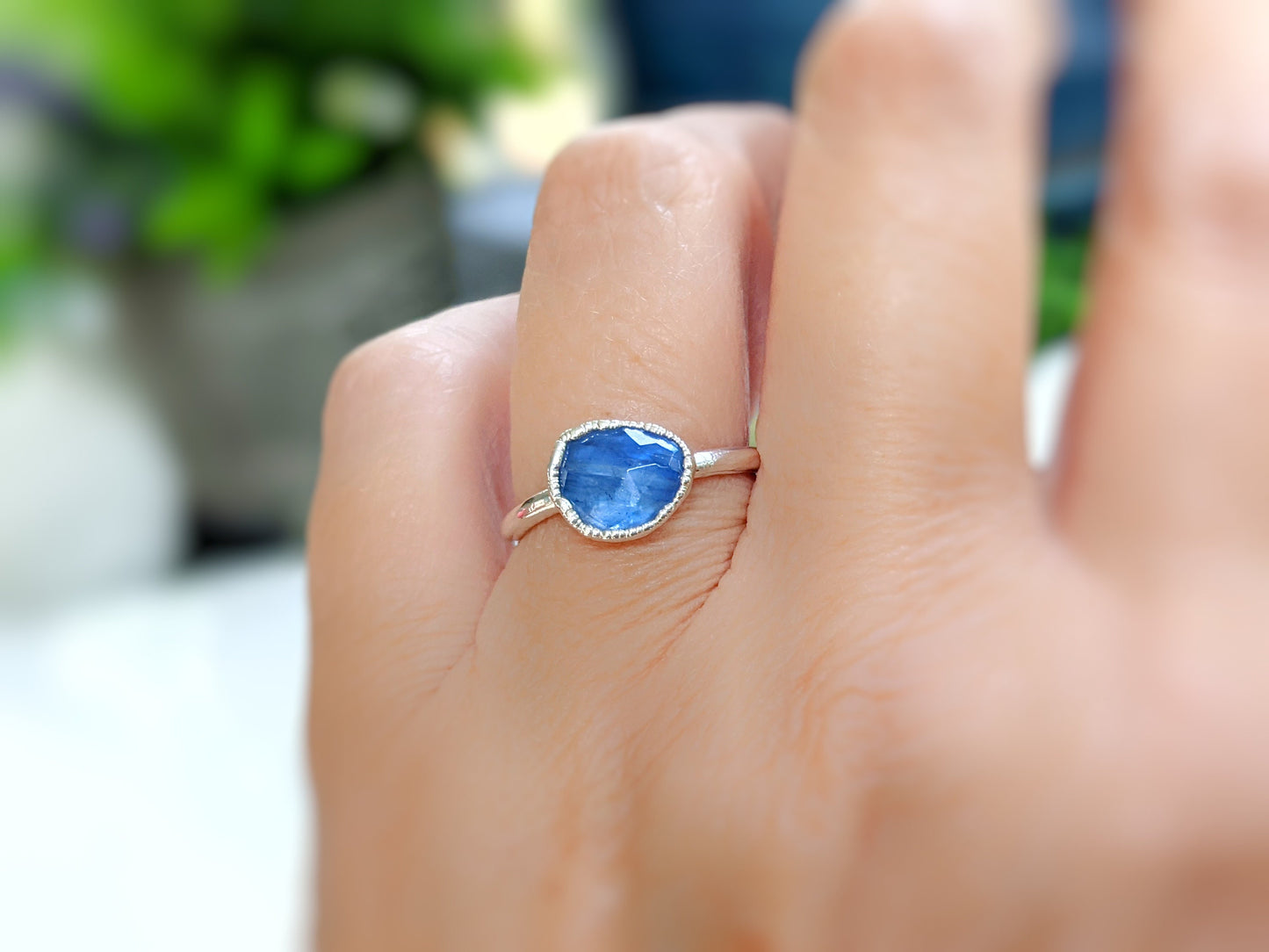 Close-up of a blue rose-cut Kyanite ring on a hand, featuring a solid gold band and sparkling gemstone.