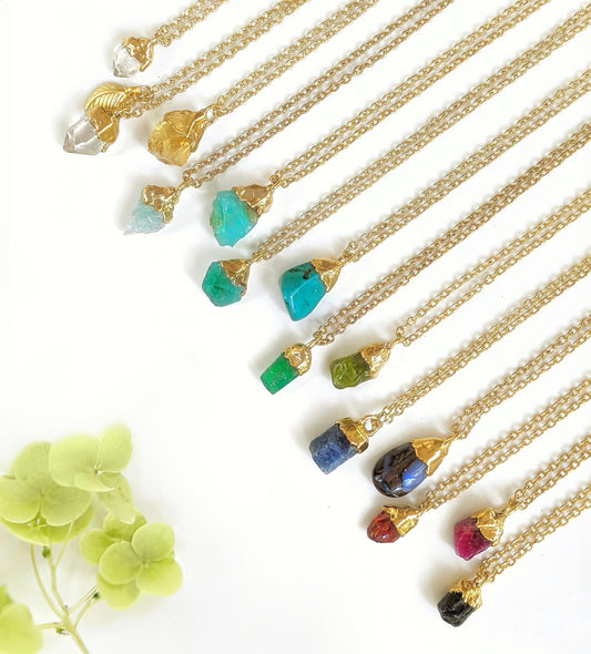 Handcrafted raw crystal and gemstone necklaces on gold-filled chains, showcasing various colorful birthstones.