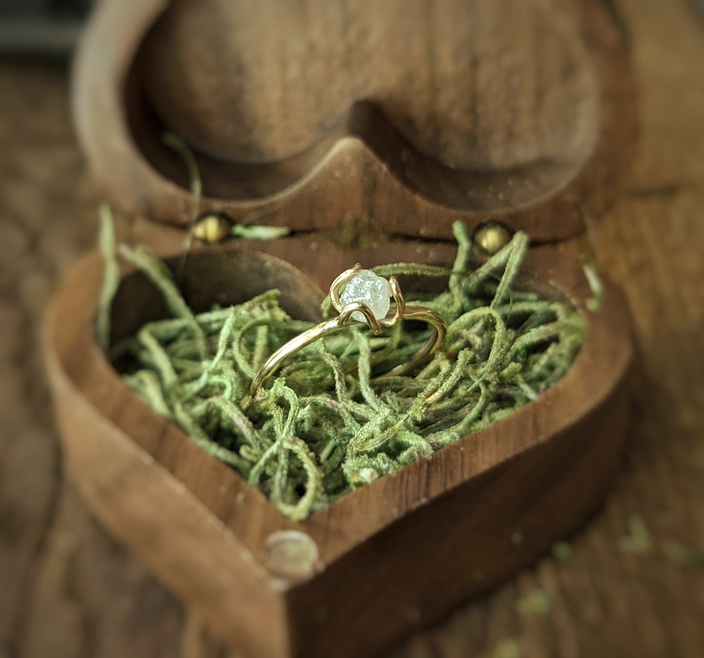 Raw diamond flower prong engagement ring displayed in a wooden heart-shaped box with green filler.