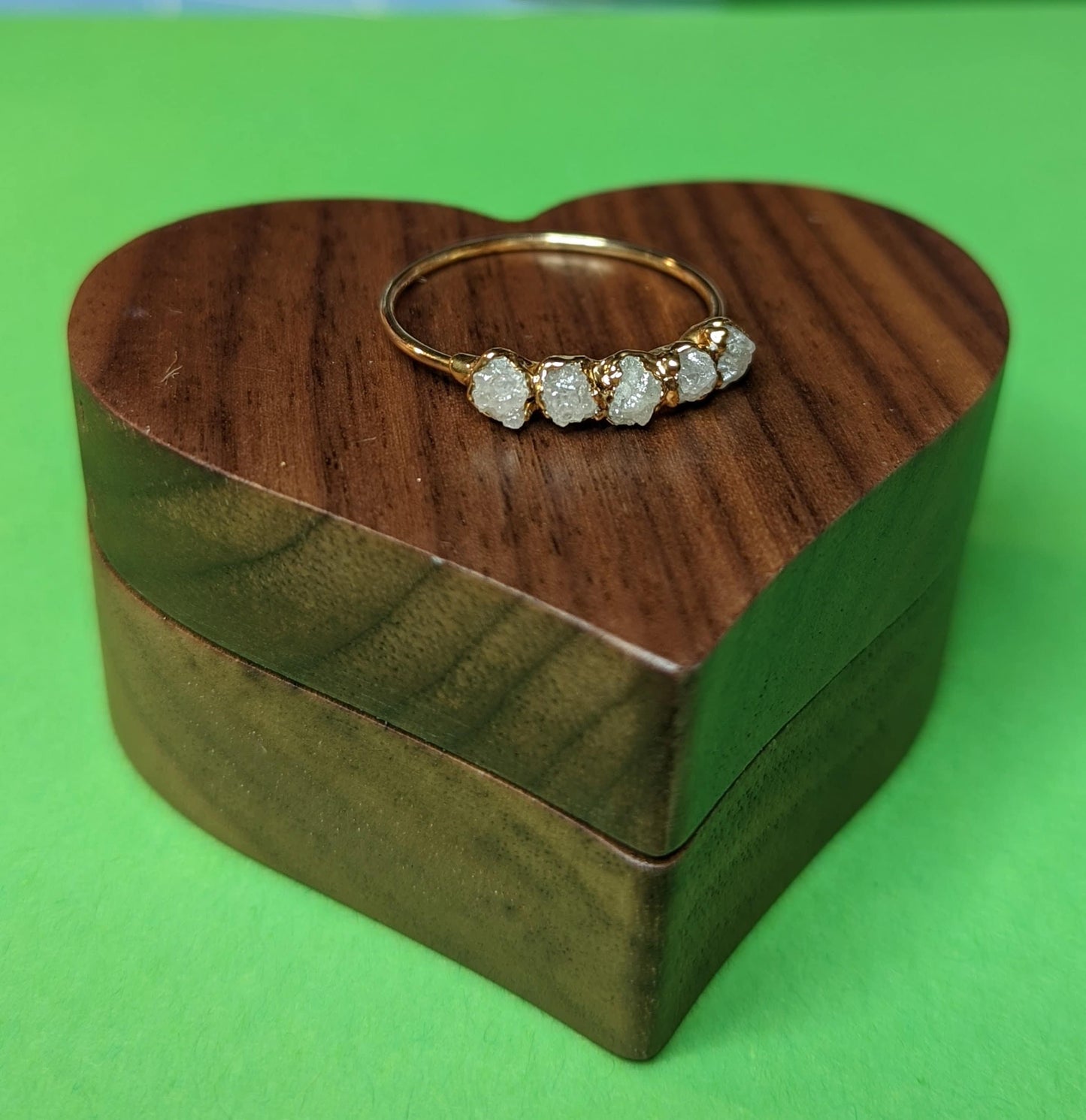Raw diamond wedding band on a heart-shaped wooden box, highlighting a unique engagement ring design.