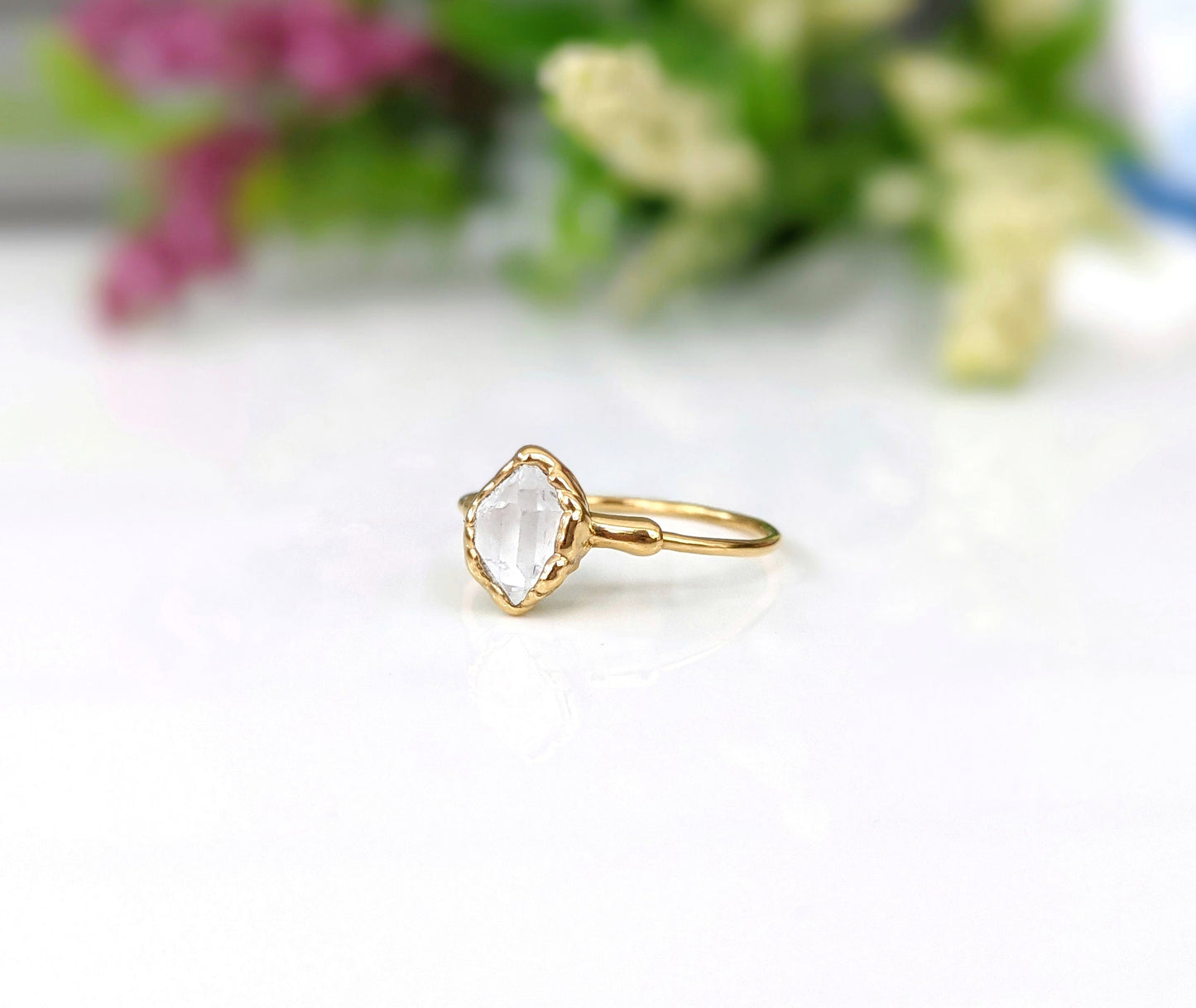 Raw Herkimer diamond engagement ring on a solid gold band with delicate floral background.