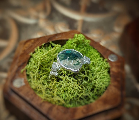Moss Agate and raw diamond twig ring on moss, showcasing a pear-shaped green agate and sparkling diamonds.