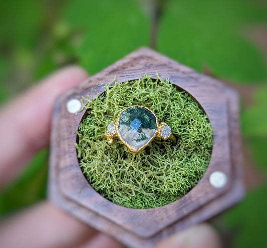 Rustic Moss Agate and raw diamond ring displayed on moss in wooden ring box, nature-inspired engagement jewelry.