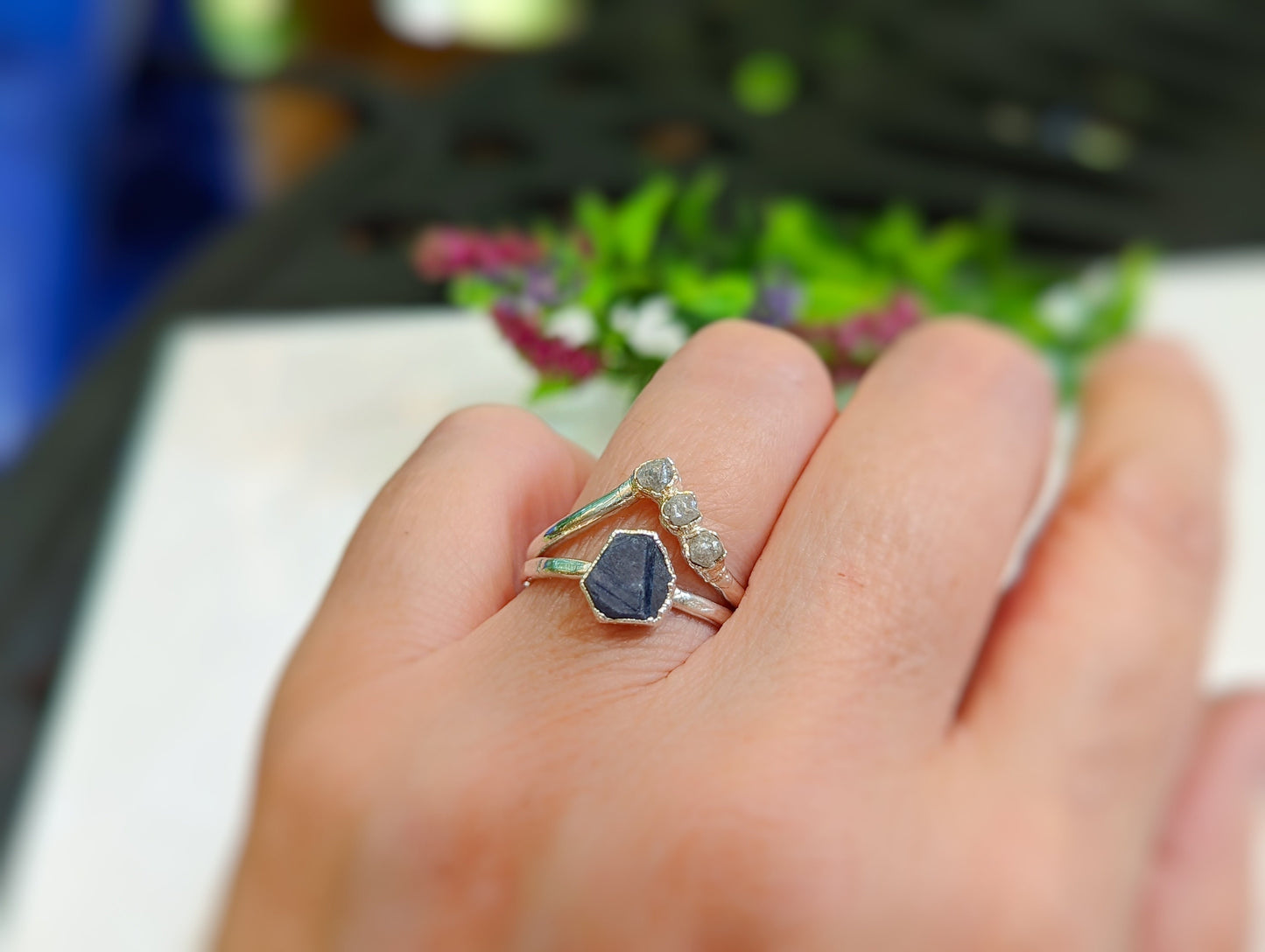 Handcrafted raw blue sapphire ring on a hand, featuring a sterling silver band and delicate stone accents.