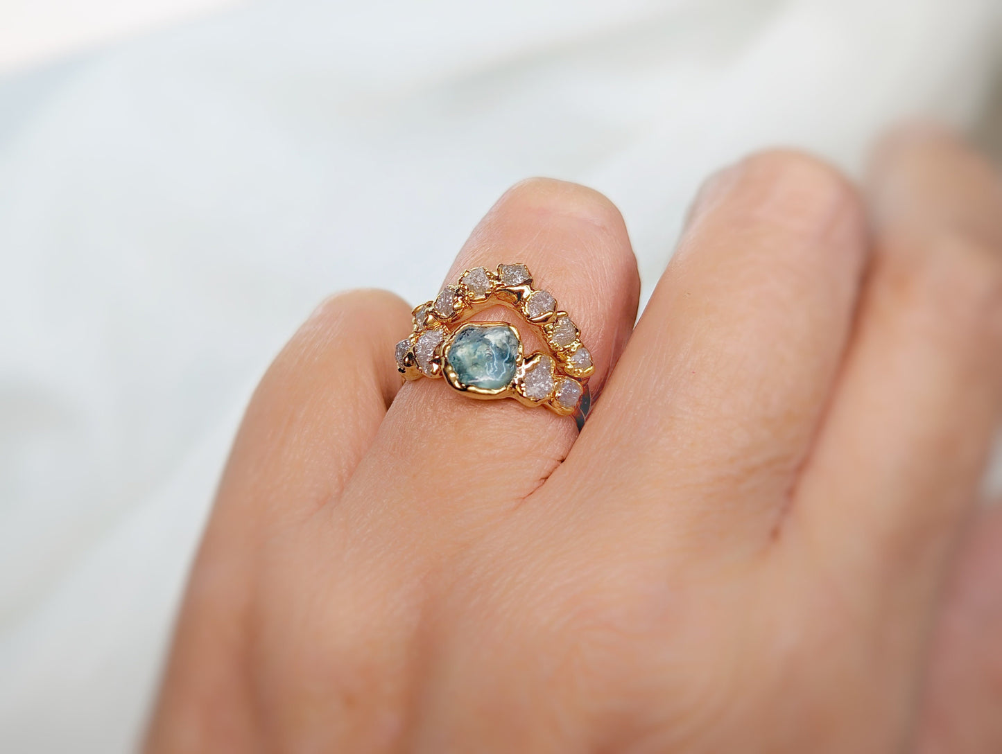 Handcrafted raw Montana Sapphire and diamond ring set on a hand, featuring a solid gold chevron band.