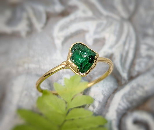Handcrafted raw green Garnet ring featuring a natural uncut stone set in a gold band, on a textured background.