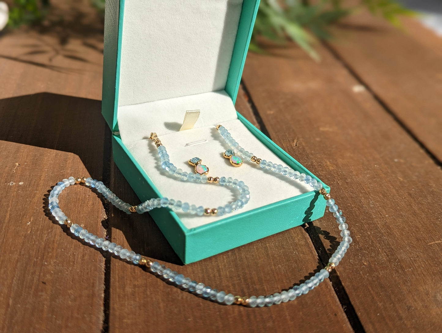 Aquamarine and Opal bridal jewelry set in a teal box, featuring earrings and a bead necklace on a wooden surface.