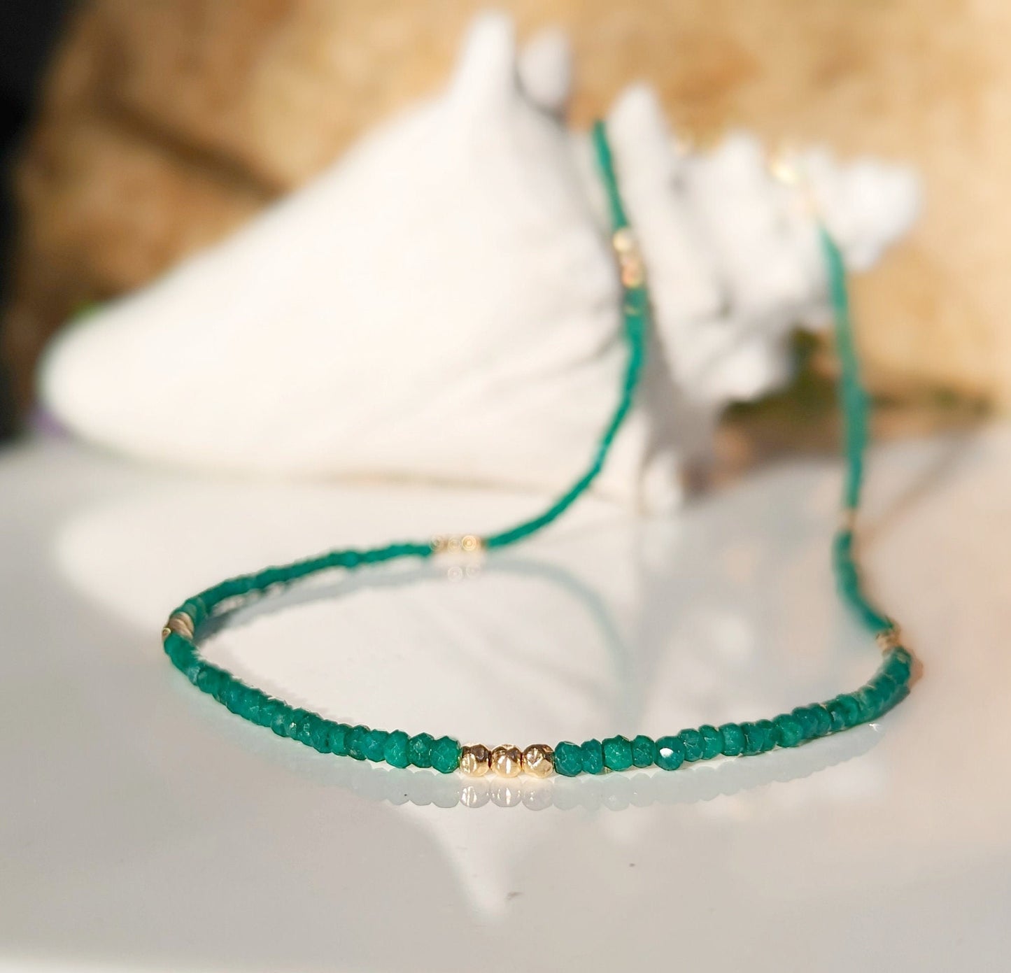 Emerald bead necklace showcasing unique green shades, symbolizing love and friendship, elegantly displayed on a reflective surface.
