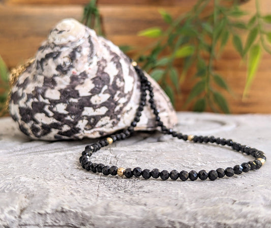 Elegant black spinel bead necklace displayed on stone surface with seashell accent.