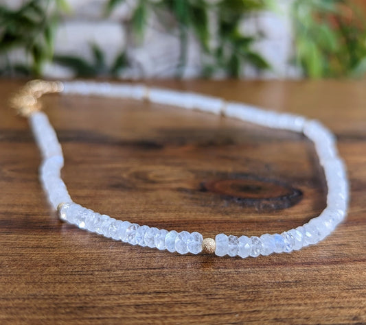 Dainty rainbow Moonstone faceted beaded necklace on wooden surface, showcasing beautiful iridescent beads.