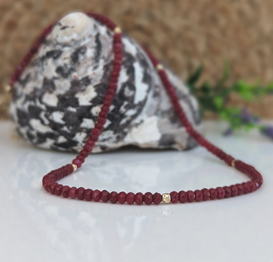 Handmade ruby beaded necklace against a natural stone backdrop, featuring deep pink and gold accents.