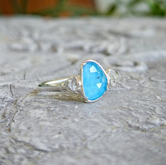 Blue Topaz and Herkimer diamond engagement ring in sterling silver on a stone surface.