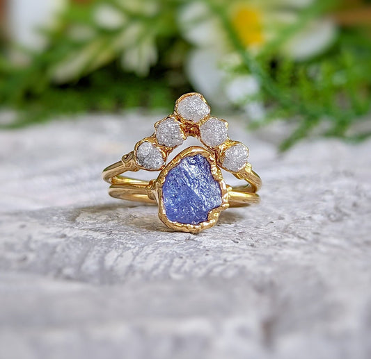 Raw Tanzanite and diamond Chevron wedding ring set on a textured surface with floral background.
