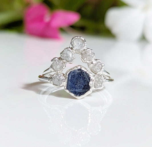 Raw sapphire and diamond wedding ring set on a reflective surface, featuring unique designs in sterling silver.