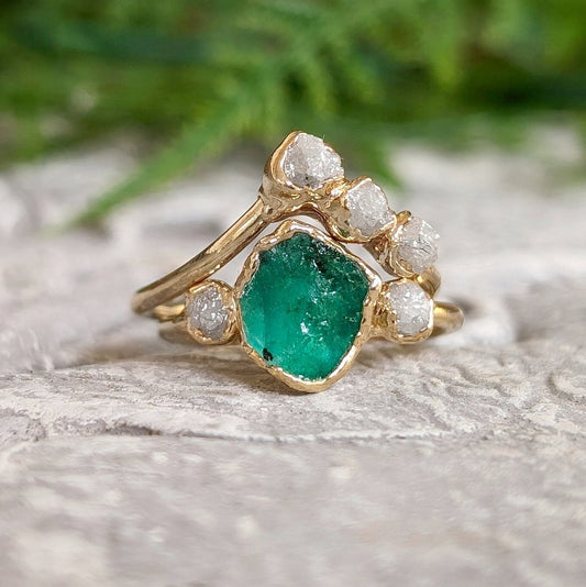 Raw Emerald and diamond Chevron wedding ring set on a natural stone background, featuring 18k Gold band.