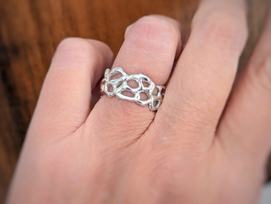 Hand wearing a Molten Silver Honeycomb ring, showcasing its unique abstract design and fluid metallic texture.