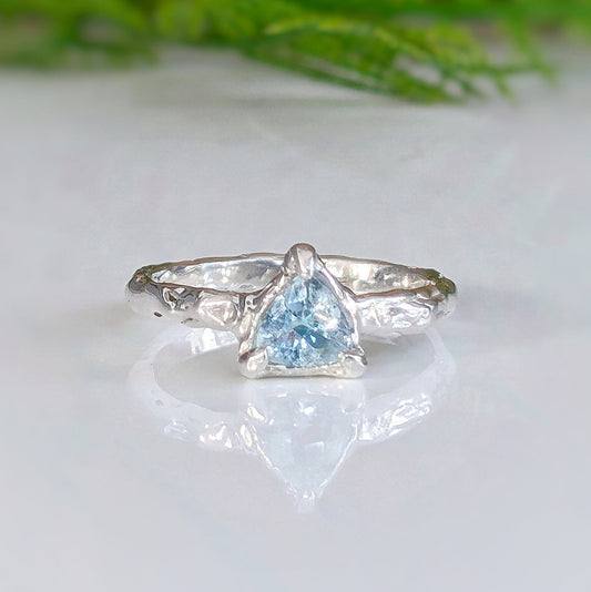 Solid silver ring featuring a trilliant aquamarine, handcrafted with an organic textured band, symbolizing timeless love.