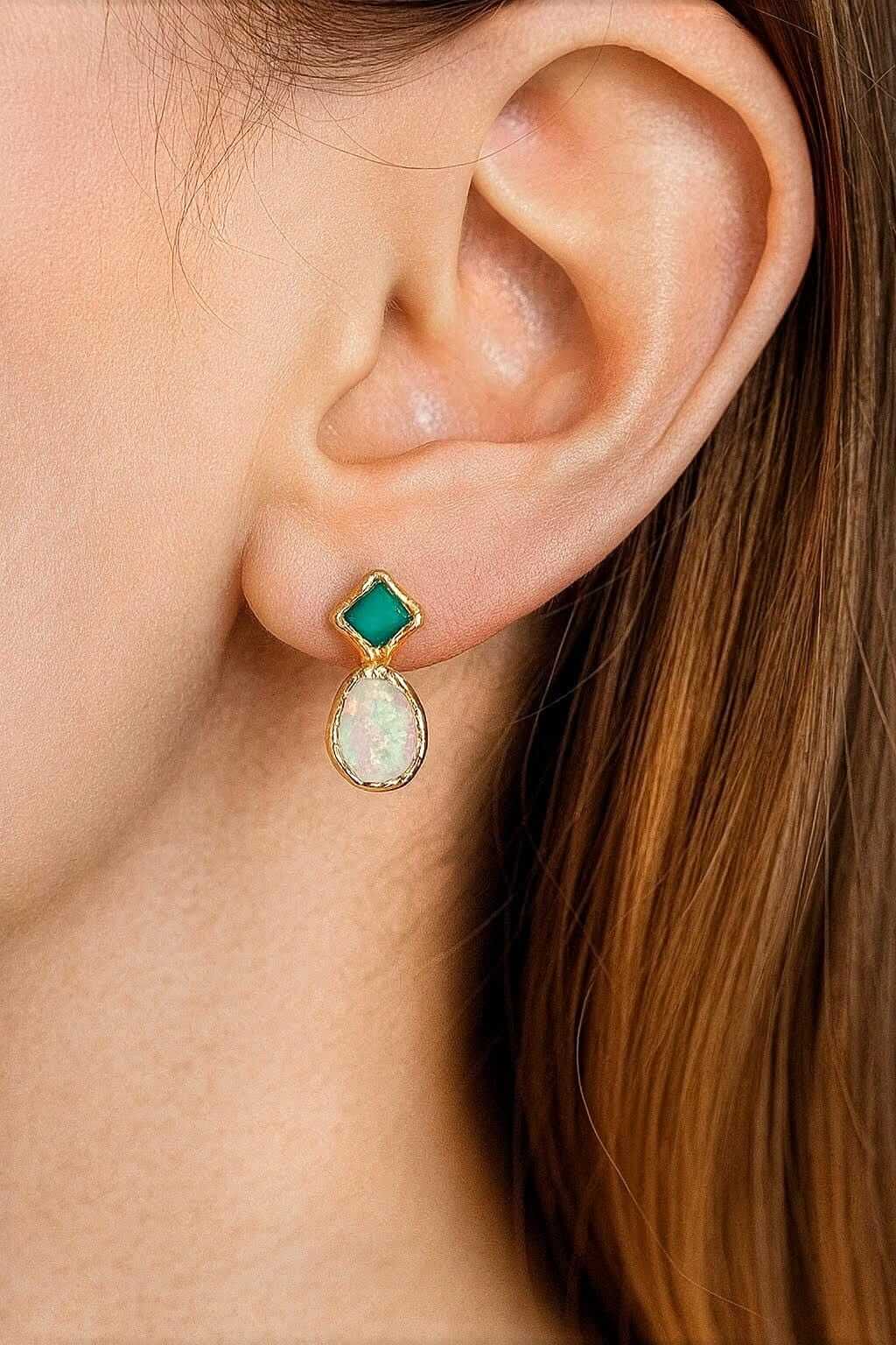 Close-up of a woman's ear wearing a gold stud earring with a green Emerald and opal gemstone.