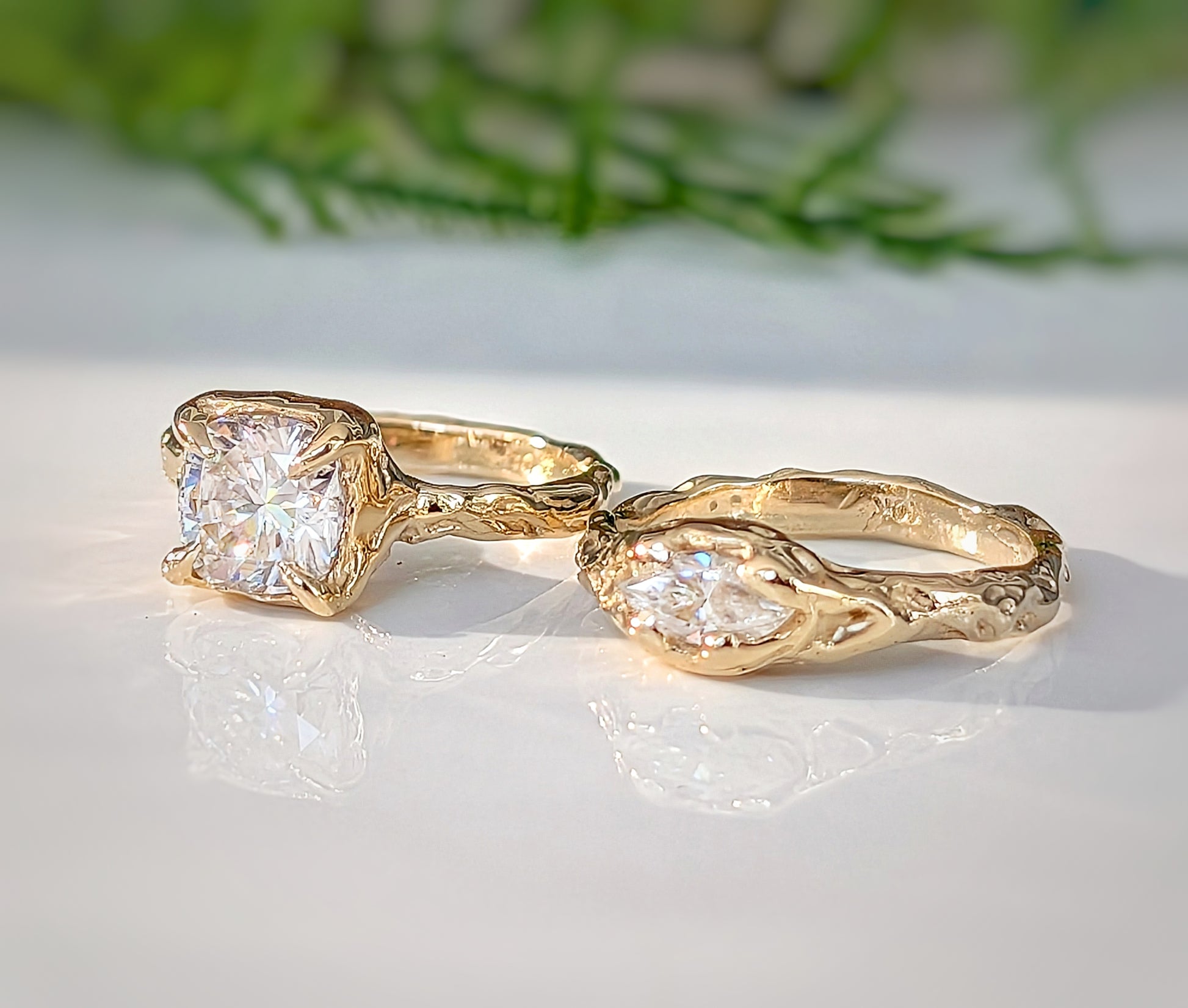 Two Gold Moissanite engagement rings, one with an 8mm Cushion gemstone, the  other with a Marquise cut Moissanite - both set in a Molten textured design