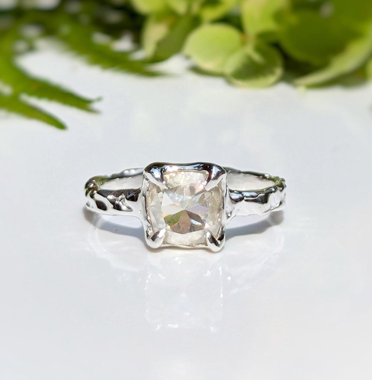 Silver Moissanite textured ring with an 8mm cushion cut gemstone, set in an organic design on a reflective surface.