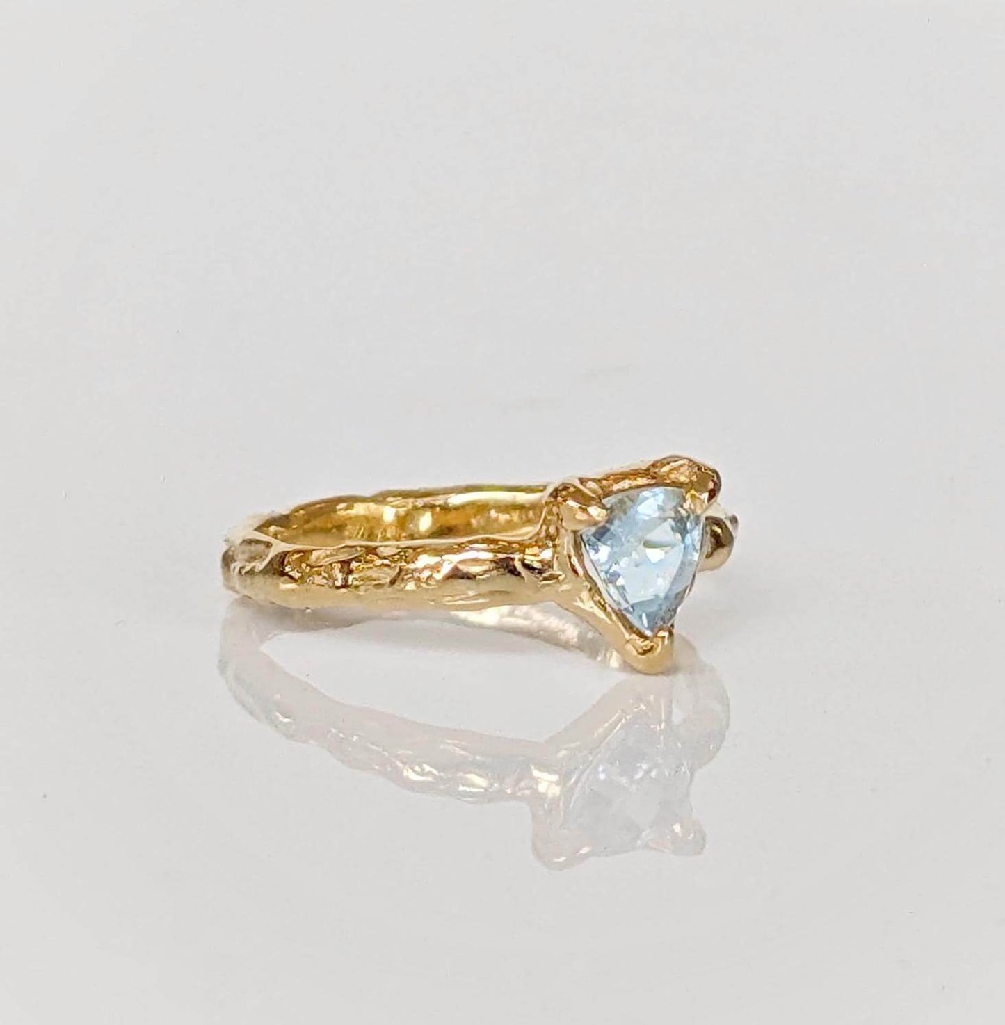 Handcrafted solid gold aquamarine ring with organic textured band, featuring a tri-shaped blue crystal.