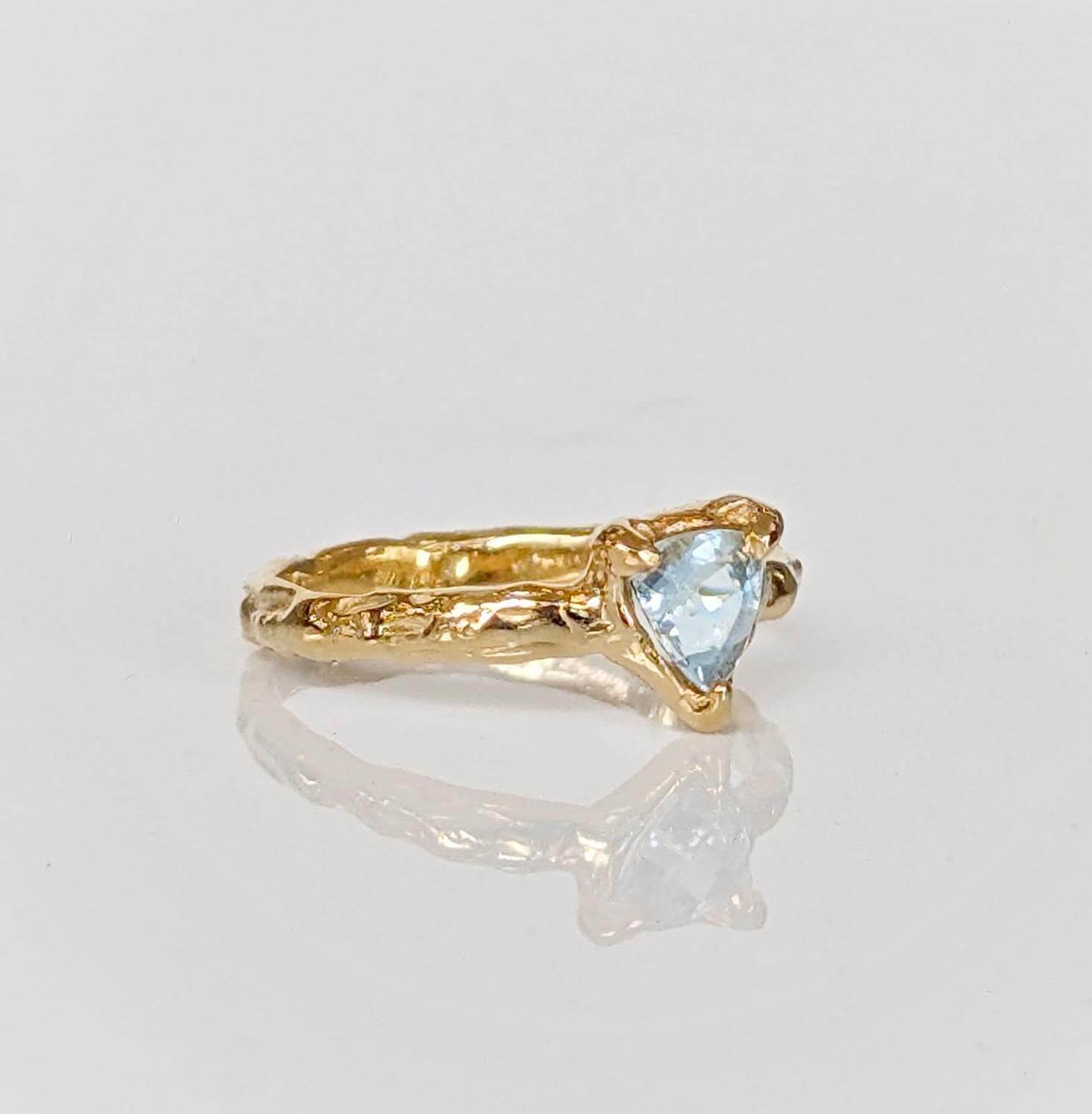 Handcrafted solid gold aquamarine ring with organic textured band, featuring a tri-shaped blue crystal.