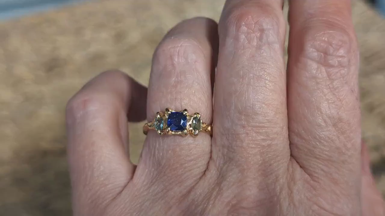 Woman's hand wearing a Square Blue Sapphire and 2 small green Tourmaline set by prongs on a textured Solid 14k Gold band