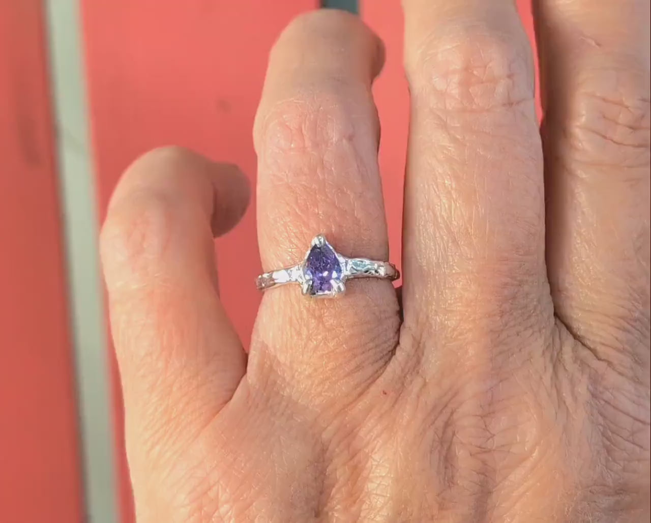 Woman's hand wearing a Pear shape Amethyst ring in Molten Silver setting