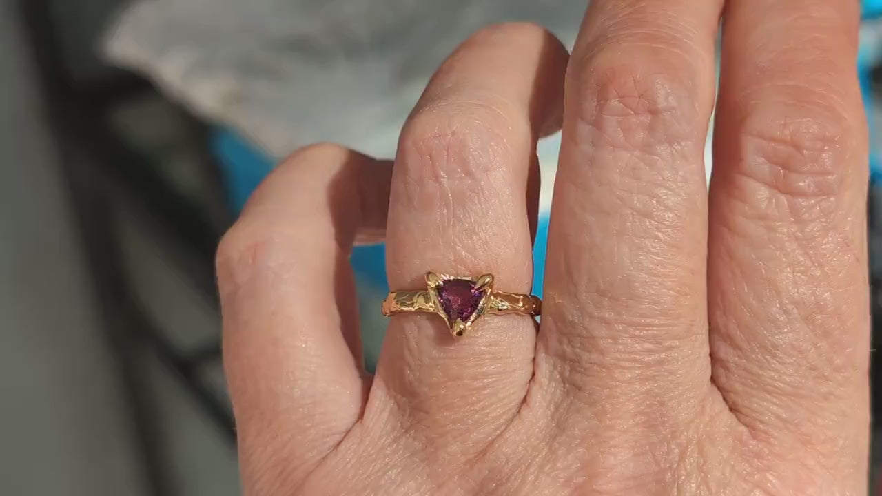 Hand with a Trilliant shape Rubellite Tourmaline set by prongs on a textured Solid 14k Gold band